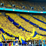 **Image:** A vibrant, slightly grainy photo of a football stadium in Ukraine, packed with passionate fans. The stands are a sea of yellow and blue (Ukrainian flag colors), with some fans holding up scarves and banners. Focus on the faces of the supporters - a mix of ages and emotions, from intense concentration to joyous shouting. Capture the energy and excitement of the crowd.